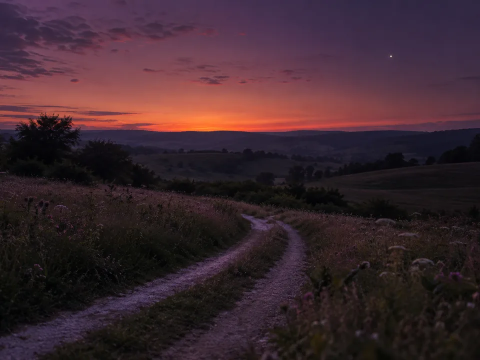 Ein Feldweg führt in der Dämmerung auf den Horizont zu, darüber der Abendstern